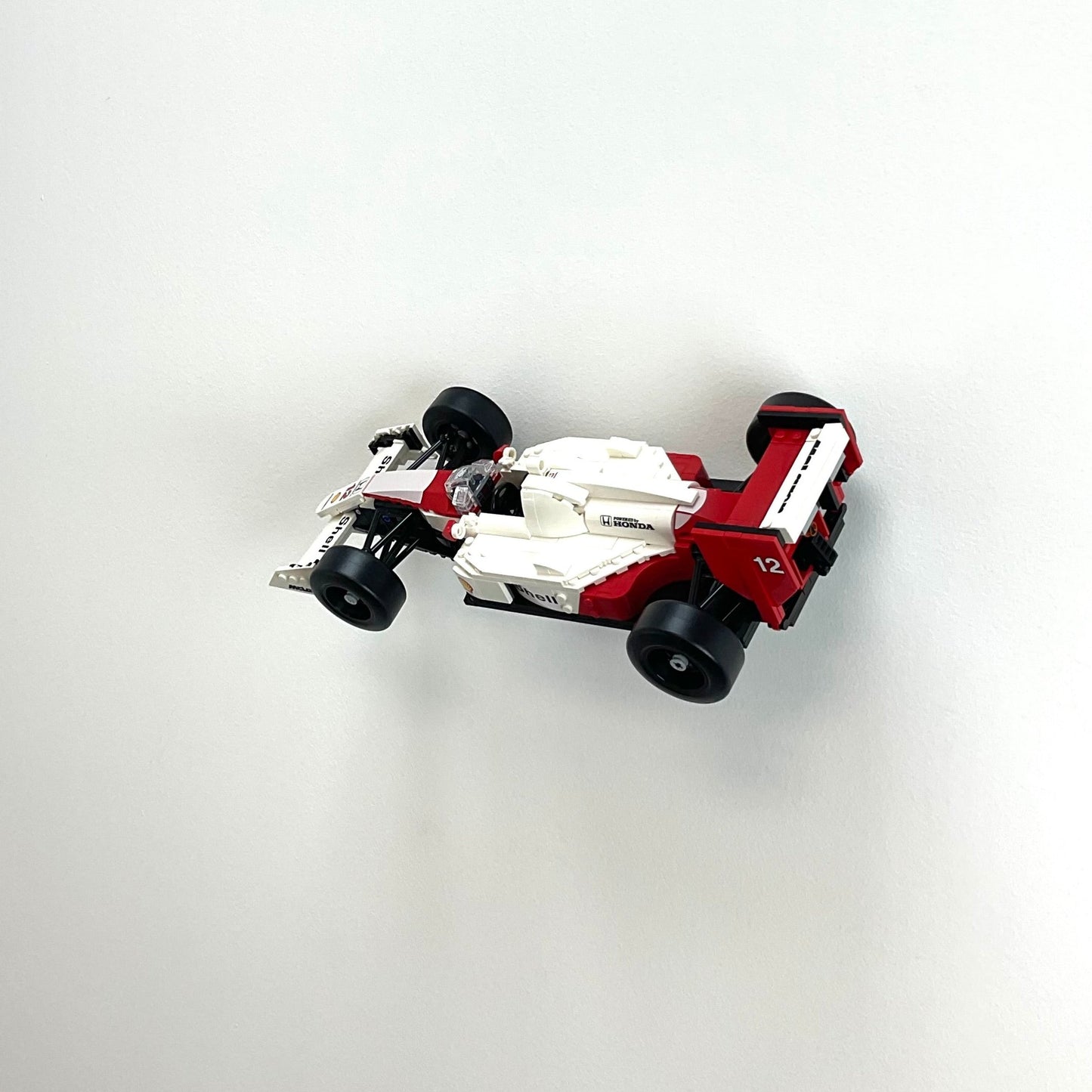 Wall display mount holding LEGO® McLaren MP4/4 & Ayrton Senna (10330) model, showcasing the car at an angled position on the wall for an eye-catching display.