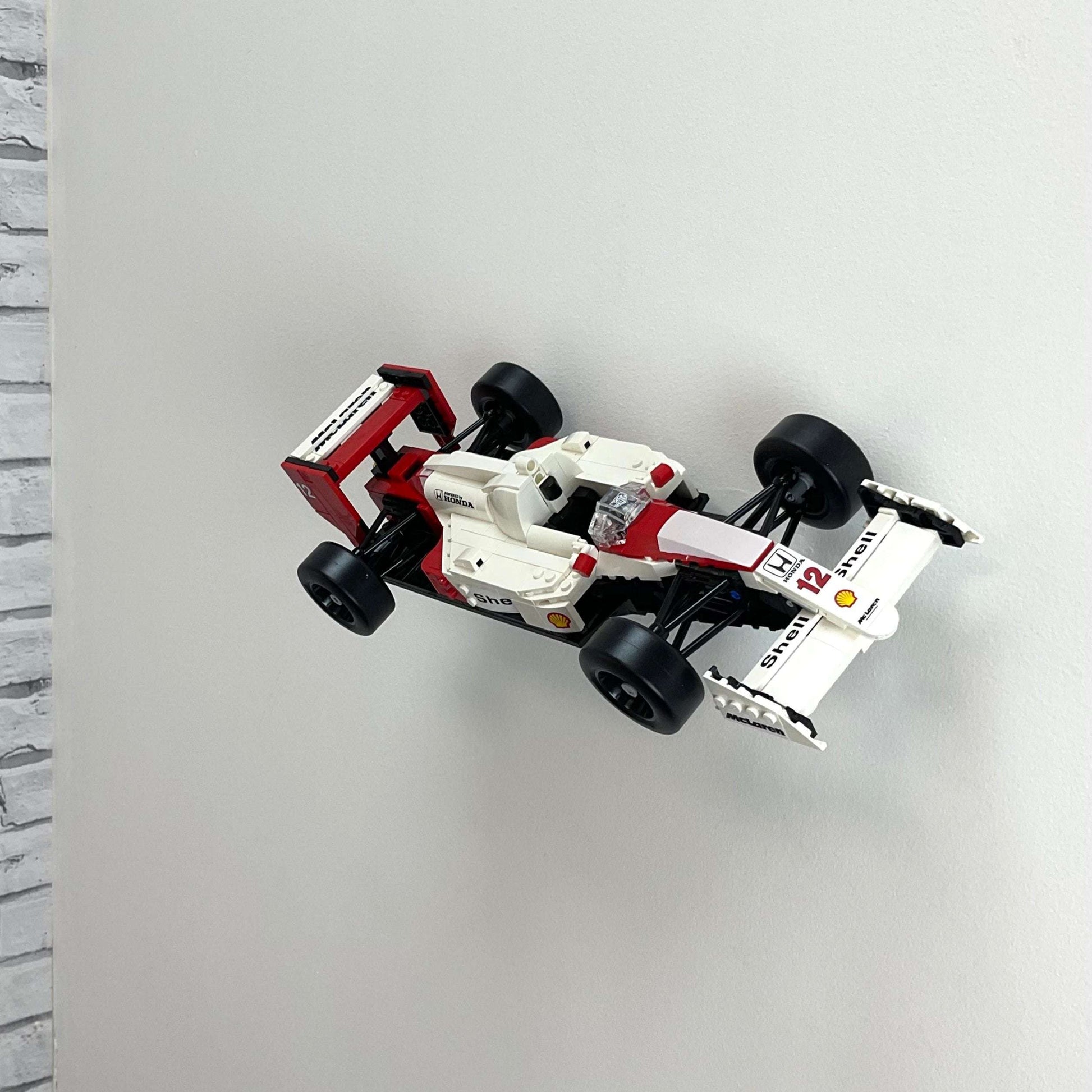 Wall display mount holding LEGO® McLaren MP4/4 & Ayrton Senna (10330) model, showcasing the car at an angled position on the wall for an eye-catching display.

