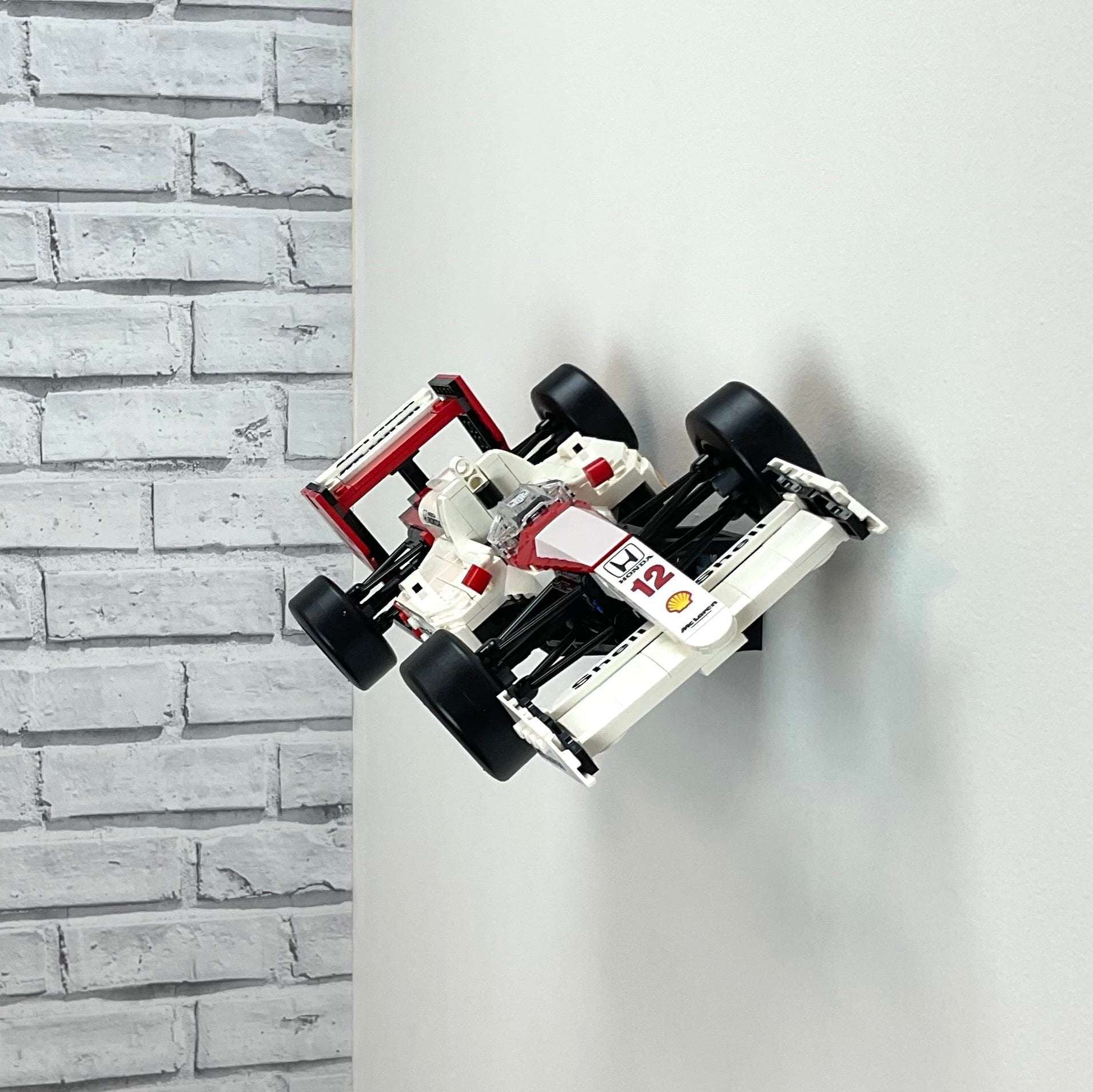 Wall display mount holding LEGO® McLaren MP4/4 & Ayrton Senna (10330) model, showcasing the car at an angled position on the wall for an eye-catching display.
