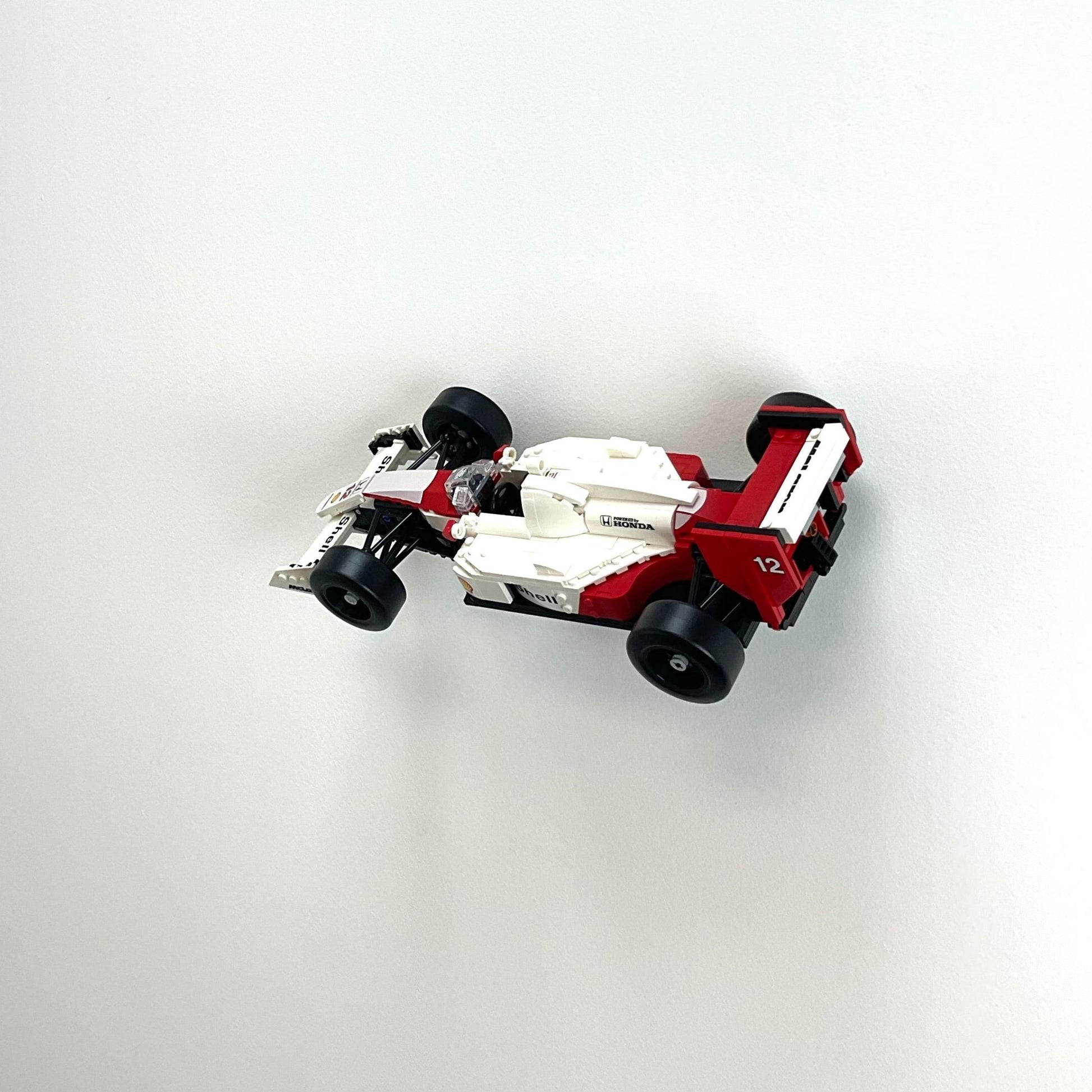 Wall display mount holding LEGO® McLaren MP4/4 & Ayrton Senna (10330) model, showcasing the car at an angled position on the wall for an eye-catching display.
